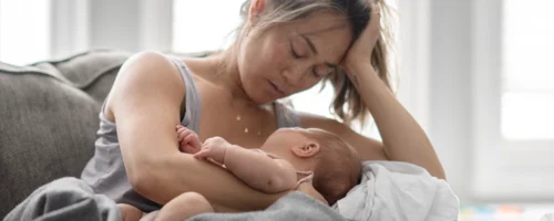 Tired and stressed mother holding her newborn while resting on her couch